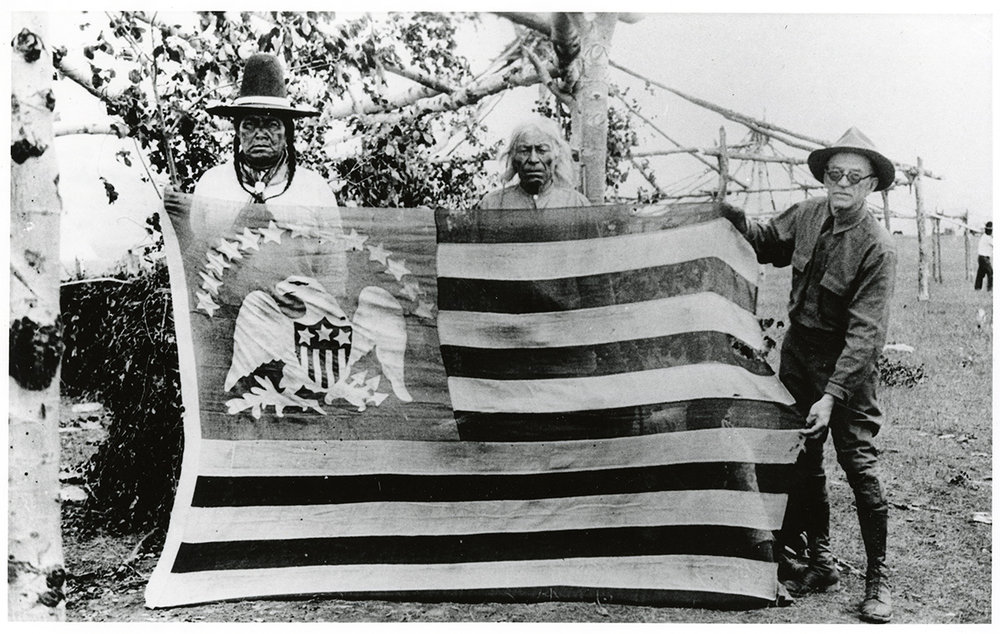Three men hold a large flag with an eagle and 13 starts on the canton