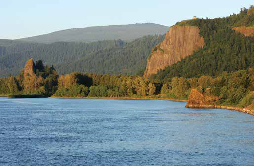 A small pointed rock next to the water and a tall cliff