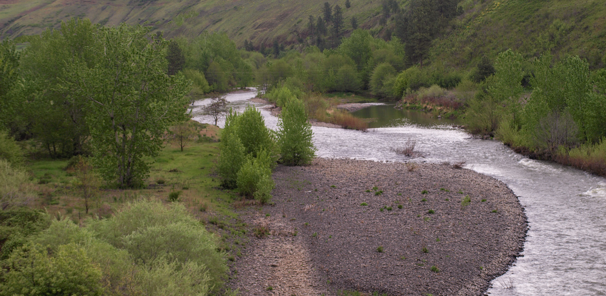 A small river flows around tall, green hills