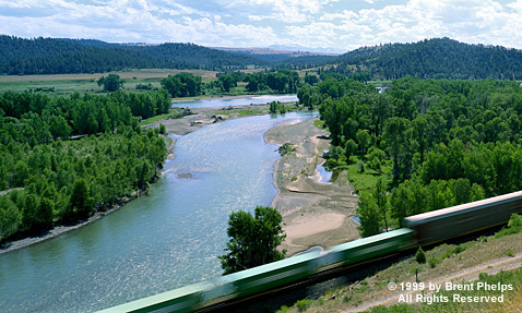 A river winds through a broad valley as a train passes