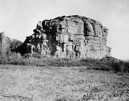 barren pillar of rock surrounded by bare ground and low bushes